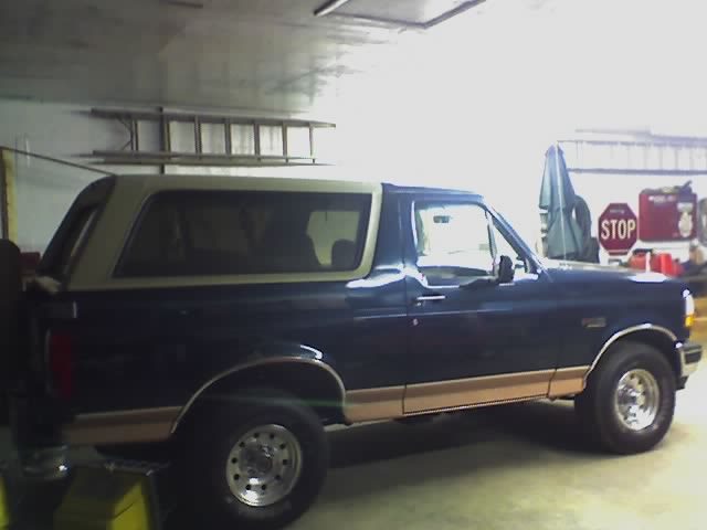 Dark blue Ford Bronco with tan two-tone lower trim and tan top, side view inside a garage