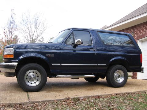 1967 Ford Mustang - This dark blue Ford Bronco is seen from the side, parked on a concrete driveway.