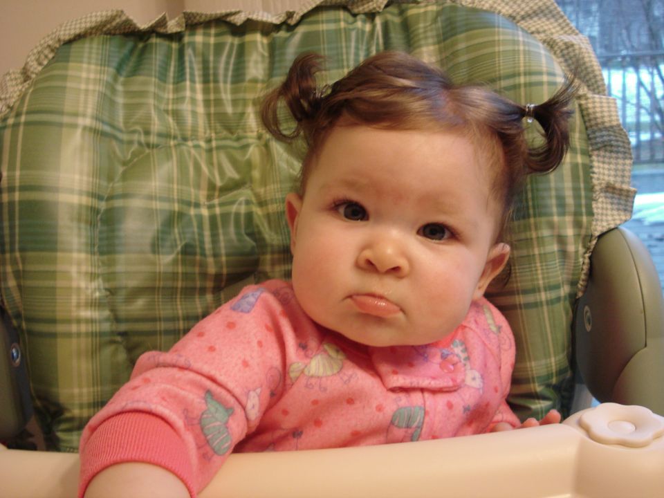 Baby in a high chair with pigtails and a pout