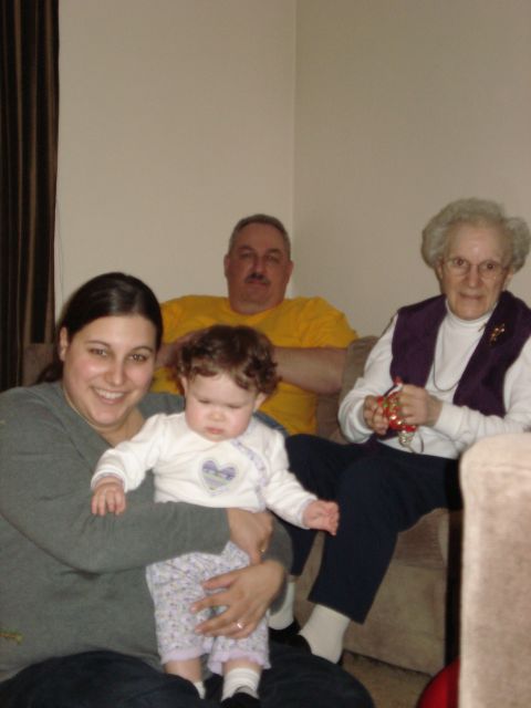 2000 Ford Crown Victoria - A family gathers on a couch, with a woman holding a baby in the foreground, a man behind them, and an elderly woman to the side.