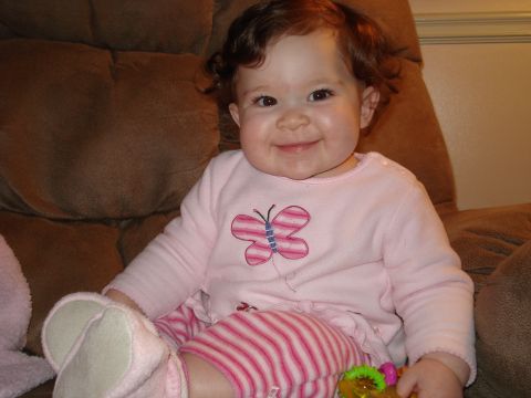 2000 Ford Crown Victoria - A smiling baby girl wearing a pink shirt with a butterfly design and pink and white striped pants sits on a brown chair.