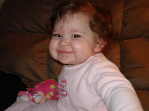 2000 Ford Crown Victoria - A baby with curly hair smiles while sitting on a brown couch with a doll.