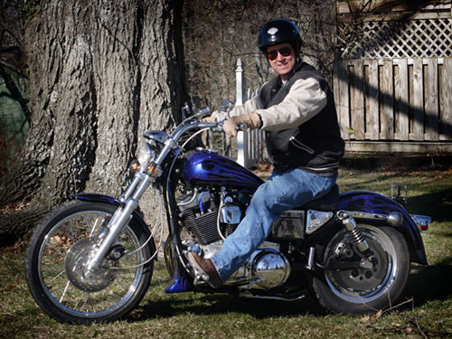 Man on blue flame-painted custom motorcycle parked on grass by a tree
