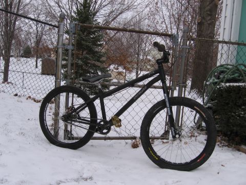1997 Ford Probe - A black Specialized bicycle rests in the snow, leaning against a chain-link fence on a cloudy day.