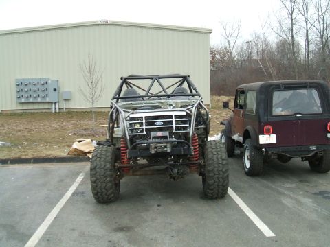 1995 Ford Bronco - A heavily modified vehicle with a custom roll cage and off-road tires is parked next to a Jeep.