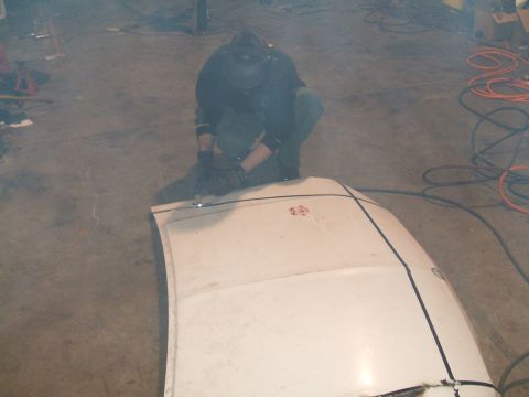1995 Ford Bronco - A person in a welding mask works on a white vehicle hood, with various tools and cords visible in the background.