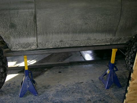 1978 Ford Bronco - The underside of a vehicle is supported by jack stands, revealing its frame and custom sliders.