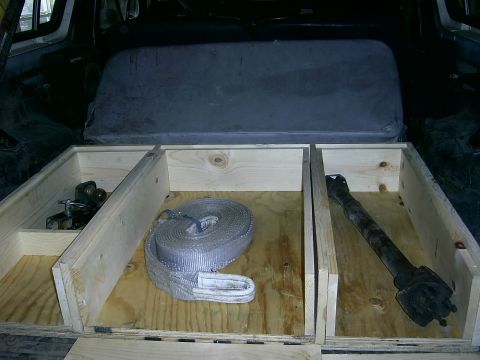 1978 Ford Bronco - Custom wooden storage compartments installed in the rear of a vehicle, holding a strap and a driveshaft.