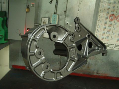 1996 Ford Bronco - A metal casting part is shown in a workshop setting, with a chart on the wall behind it.