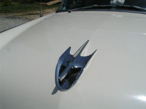 1956 Ford Fairlane - A chrome hood ornament with a pointed design is visible on the hood of a white 1956 Ford Fairlane.