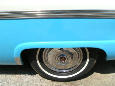 1956 Ford Fairlane - The rear wheel of a classic two-tone blue and white vehicle is visible, a whitewall tire and chrome hubcap.