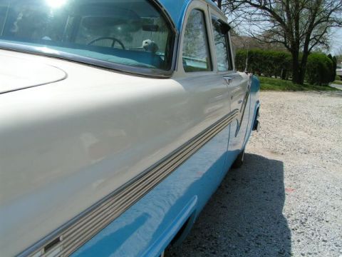 1956 Ford Fairlane - The side profile of a classic two-tone sedan is captured from a low angle, highlighting its chrome trim and body lines.