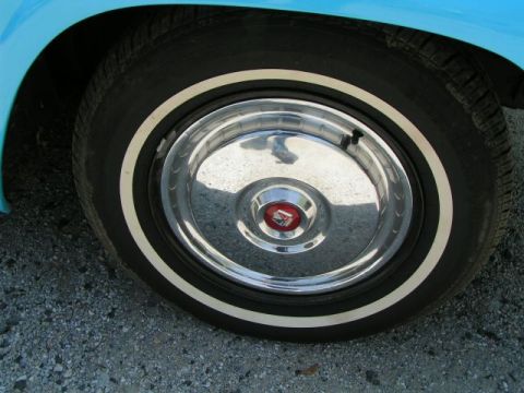 1956 Ford Fairlane - Close-up of a blue car's wheel, a whitewall tire and a chrome hubcap with a red emblem.