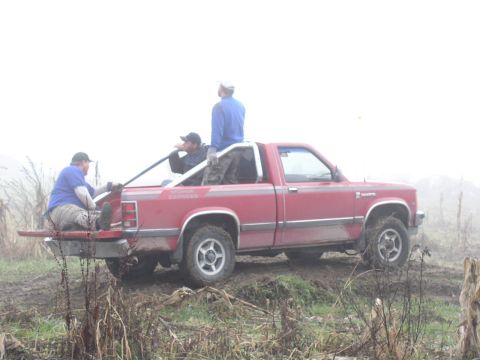 Red Dodge Dakota pickup in a foggy field with three men sitting and standing in the bed
