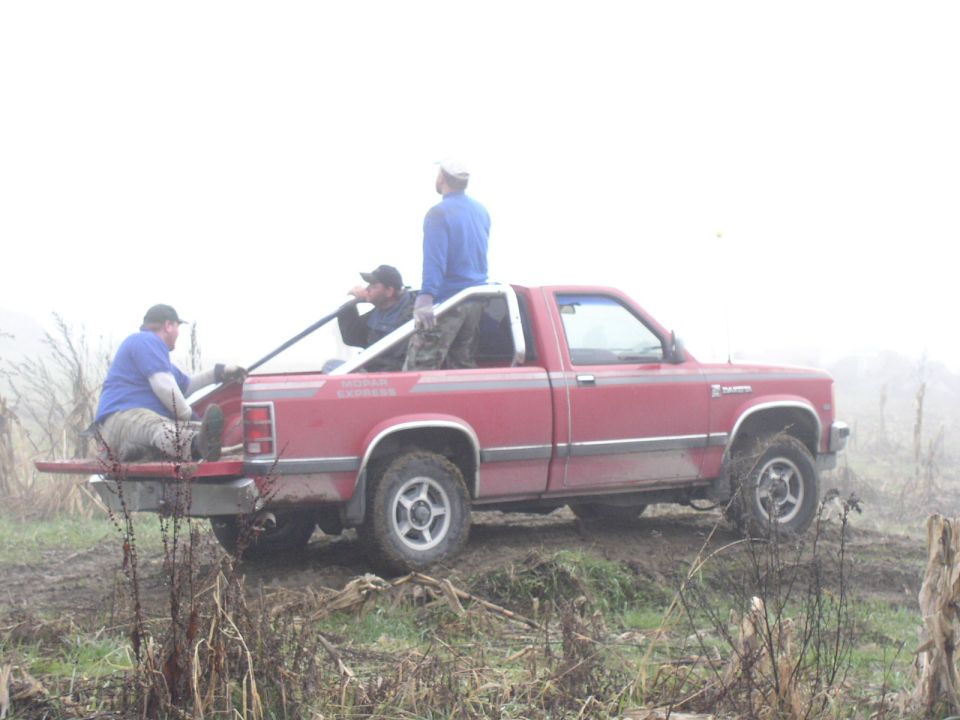 Red Dodge Dakota pickup in a foggy field with three men sitting and standing in the bed