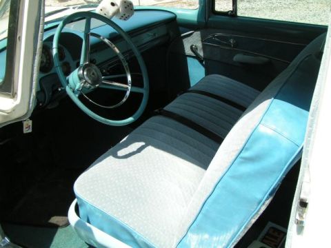 1956 Ford Fairlane - The interior of a vintage car features a turquoise steering wheel and two-tone blue and white seats.
