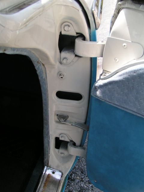 1956 Ford Fairlane - View of car door hinges and latch mechanism, with blue and white interior panels visible.
