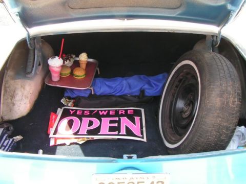 1956 Ford Fairlane - The trunk of a car is filled with a tray of food, a spare tire, and a sign that says 'Yes, we're open'.
