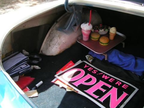 1956 Ford Fairlane - The trunk of a car contains a tray with fake burgers, a milkshake, and ice cream, along with a broom and an "Open" sign.