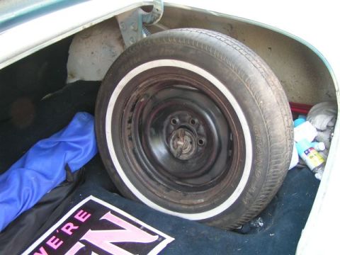 1956 Ford Fairlane - Spare tire with whitewall in trunk, next to a blue cloth and a mat with text. Other items are visible in the background.