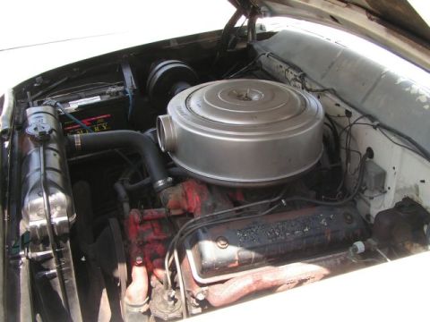 1956 Ford Fairlane - The engine compartment of a classic car shows a large air cleaner assembly and battery.