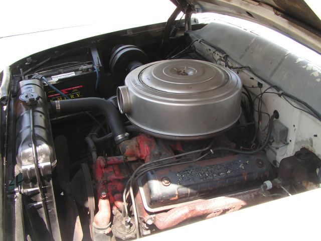 car engine bay with large round air filter, battery, and radiator visible