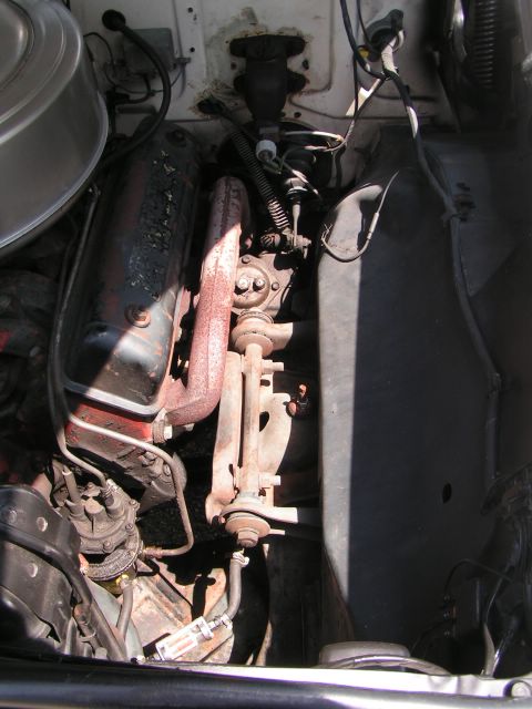 1956 Ford Fairlane - The engine bay of an older vehicle shows a V8 engine with visible hoses, wires, and exhaust components.