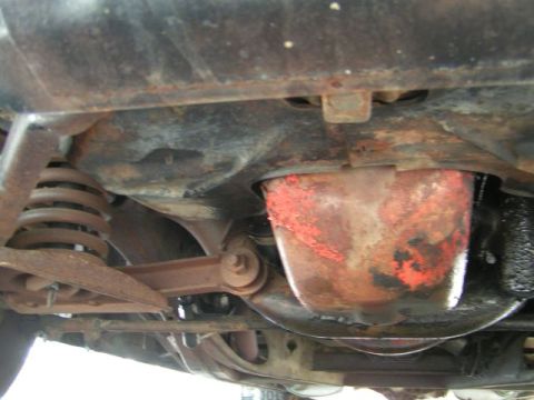 1956 Ford Fairlane - The underside of a 1956 Ford Fairlane reveals its front suspension components and a rusty oil pan.