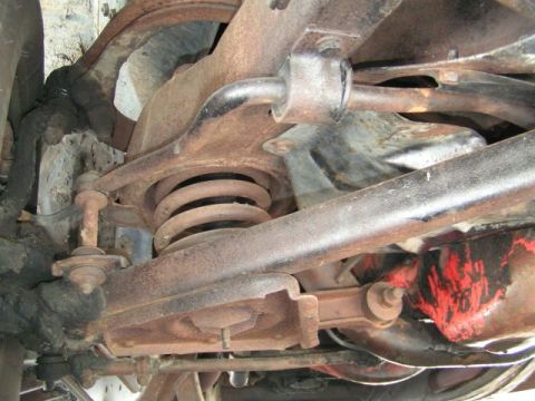 1956 Ford Fairlane - Close-up view of the rusty undercarriage suspension system, showing a coil spring and various metal linkages.