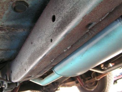 1956 Ford Fairlane - The undercarriage of a vehicle shows a light blue exhaust pipe and a rusted frame, with no visible year identification.