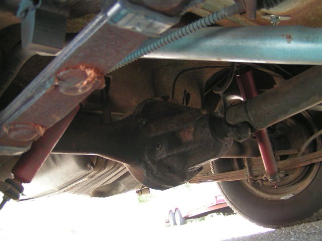 Underside view of a rusty rear axle, leaf springs, and red shock absorbers