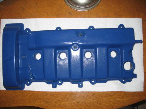 1993 Ford Probe - A blue valve cover is shown on a wooden surface, with a watermark indicating it is from Supermotors.net.