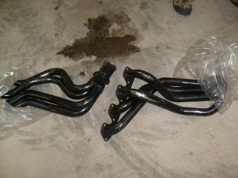 1995 Ford C-150 (Centurion Conversions) - Exhaust headers are laid out on a concrete surface, with one set partially covered in plastic.