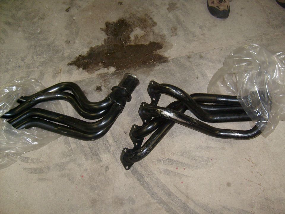 Pair of black long-tube V8 headers unwrapped on a concrete garage floor
