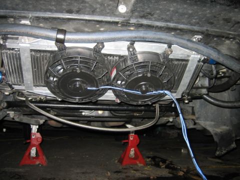 1996 Ford Thunderbird - The underside of a vehicle shows a radiator assembly with dual electric fans and visible wiring, resting on jack stands.