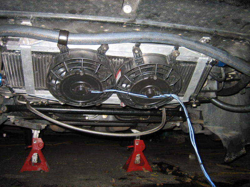 Underside view of a car's radiator with two electric fans and blue wiring, supported by red jack stands