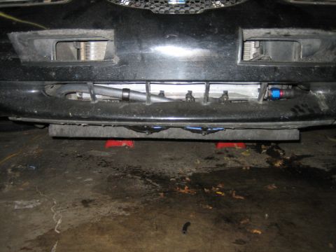 1996 Ford Thunderbird - The front of a car is raised on jack stands, revealing an intercooler and modified plumbing beneath the bumper.