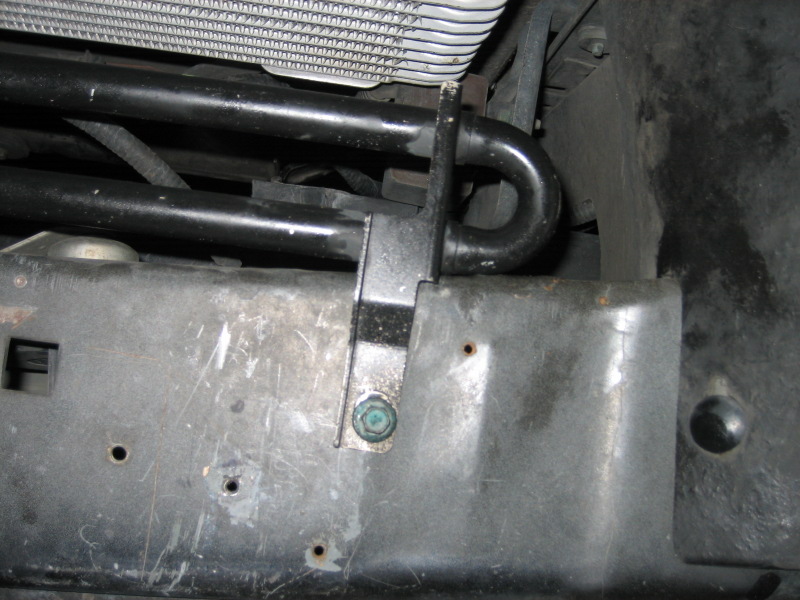 Close-up of a vehicle's front bumper area, showing metal bracing, black hoses, and part of the radiator