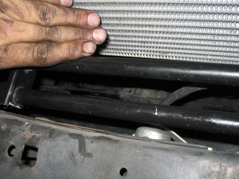 Hand touching car radiator, showing black support bars and frame below