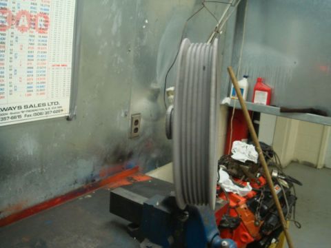 1996 Ford Bronco - A pulley is secured in a vise, with a partial engine and a wall chart visible in the background.