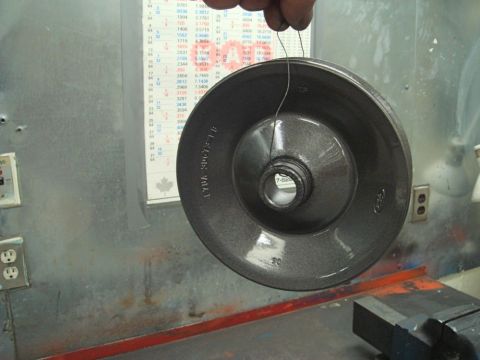 1996 Ford Bronco - A metallic pulley is held by wire in front of a chart and a metal wall.