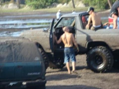 1995 Ford Bronco - People are gathered around two muddy off-road vehicles in a wet, outdoor environment.