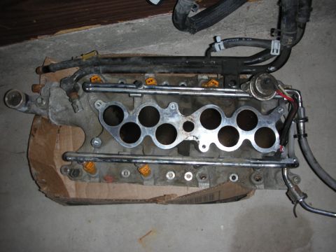 1998 Ford Crown Victoria - Aluminum lower intake manifold with fuel rails, injector ports and braided lines on a cardboard surface.
