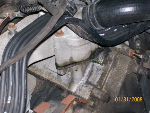 1995 Mercury Grand Marquis - Tight engine-bay close-up of a grimy aluminum accessory housing bolted to the block, surrounded by black rubber hoses, a large ribbed coola…