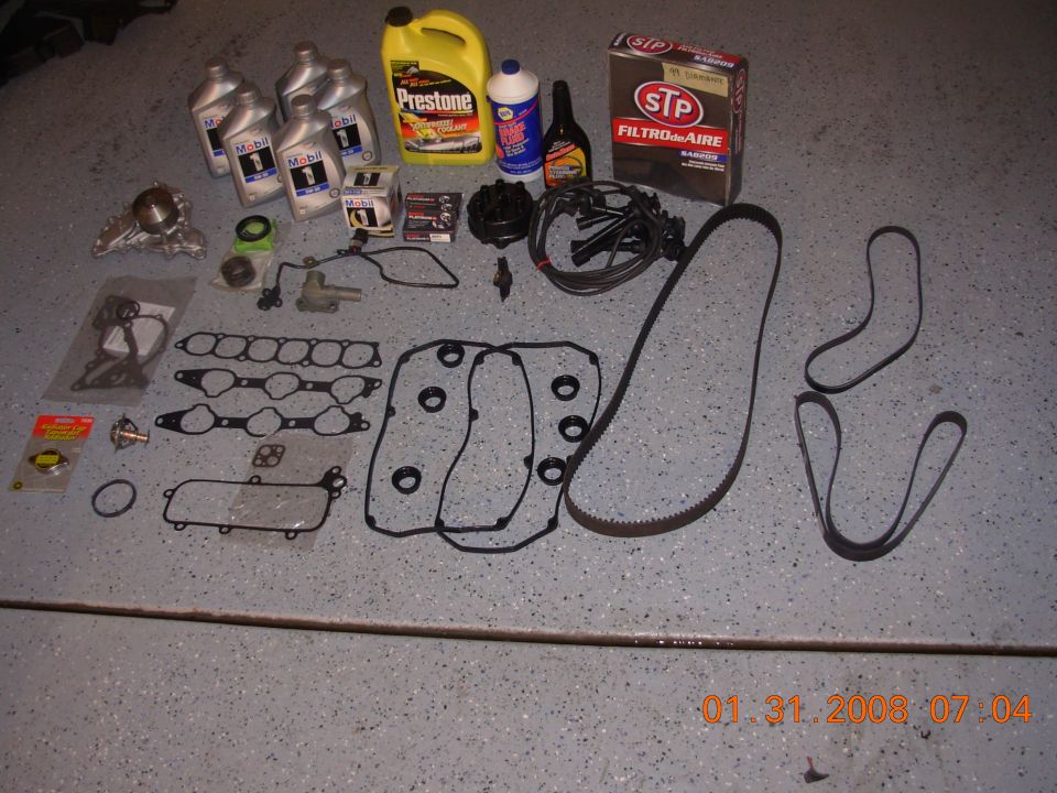 Engine parts including gaskets, belts, oil, and coolant laid out on a floor