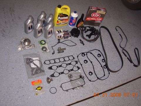 1995 Ford Taurus - A collection of engine maintenance parts and fluids are organized on a speckled floor, ready for installation.