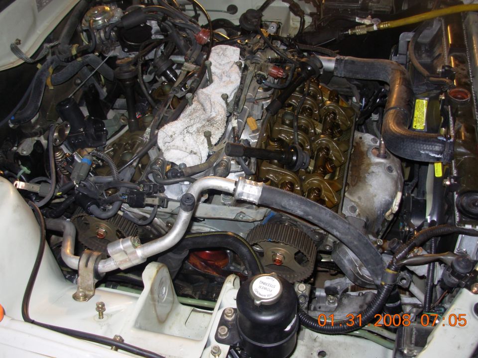 Engine with exposed valve cover, hoses, and timing gears. White cloth is on top of engine components