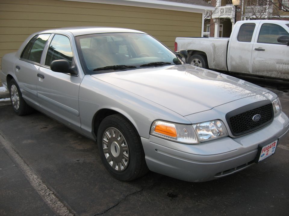 Silver sedan parked on asphalt, front 3/4 view. A white pickup truck is visible behind it