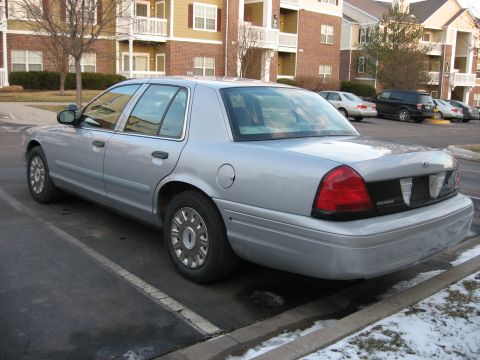 2004 Ford Crown Victoria - A silver 2004 Ford Crown Victoria is parked in a lot with snow on the ground and apartment buildings behind it.