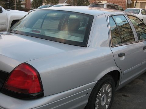 2004 Ford Crown Victoria - Rear view of a silver sedan, showing its taillight and quarter panel, with a white pickup truck partially visible.